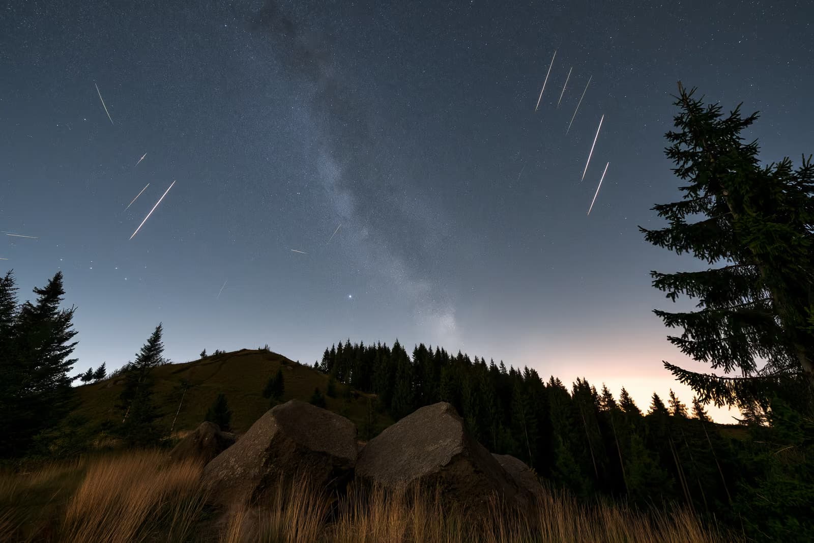 A night sky over a dark German countryside with meteor streaks and a faint band of stars overhead.