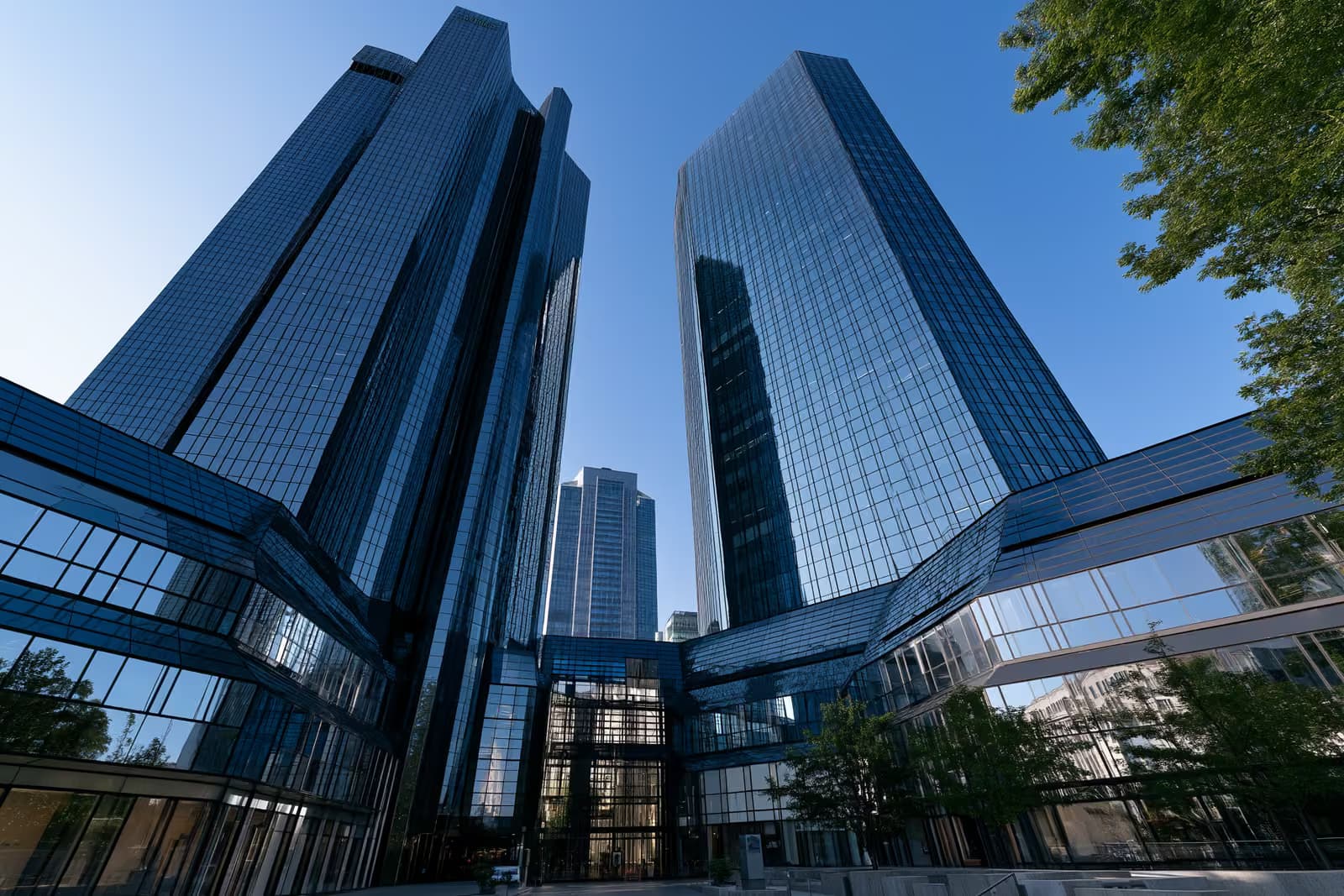 Twin glass banking towers in Frankfurt gleaming against a bright blue sky seen from below.