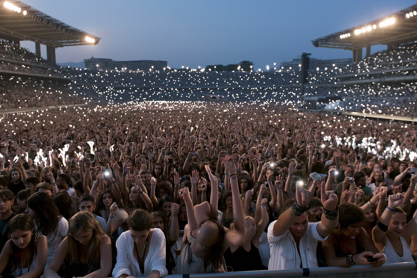 A large stadium crowd lit by evening light during a summer concert in Munich.