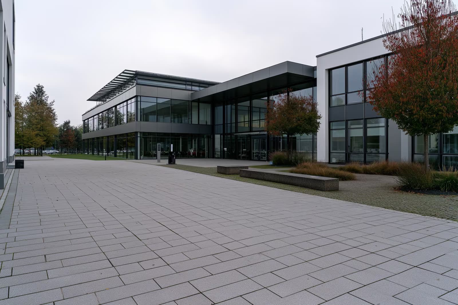 A modern German employment agency building with a wide empty paved forecourt under an overcast sky.