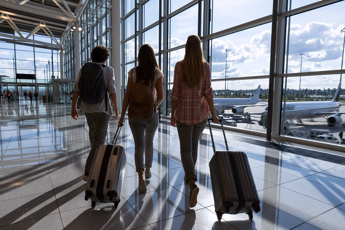 Travelers walking through a bright modern airport terminal with large windows.
