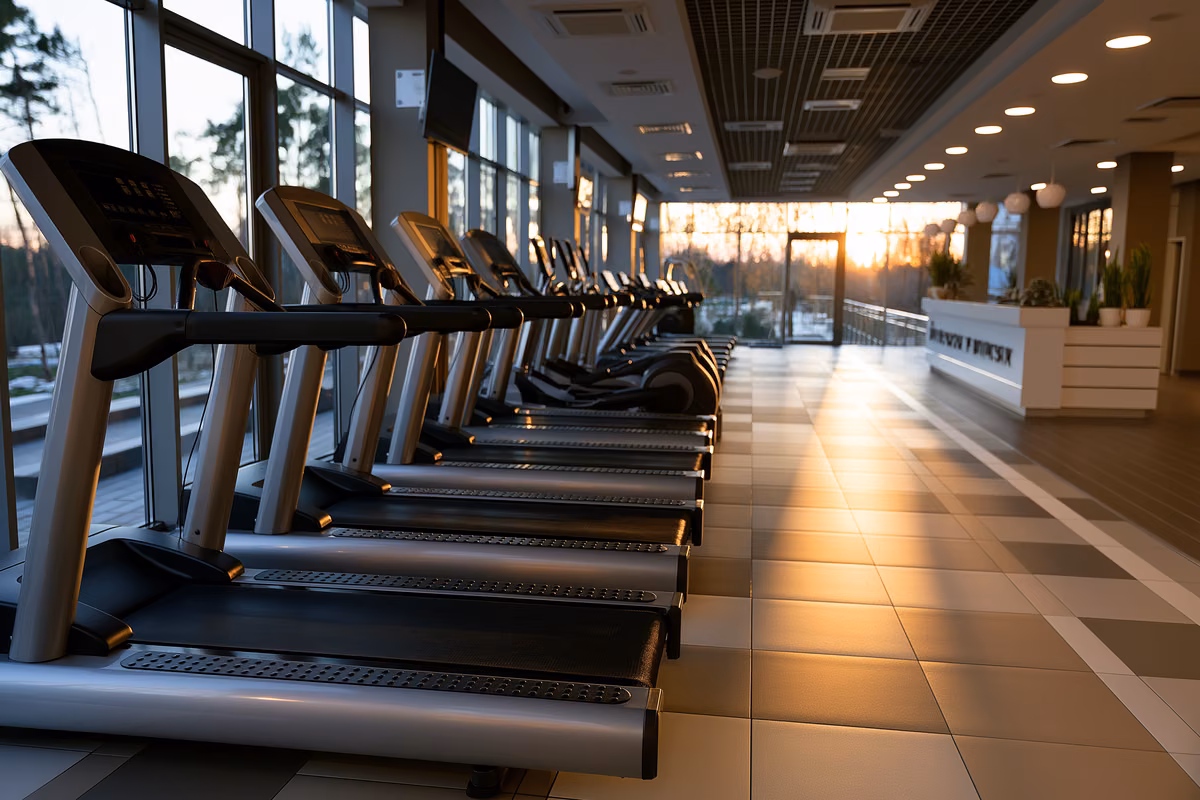 Rows of empty treadmills in a modern gym at dusk with the membership desk blurred in the background