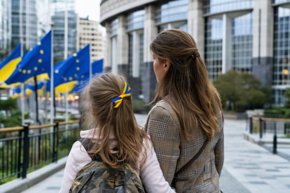 A Ukrainian mother and daughter look at EU flags outside a European institution building after the Ukraine temporary protection extension