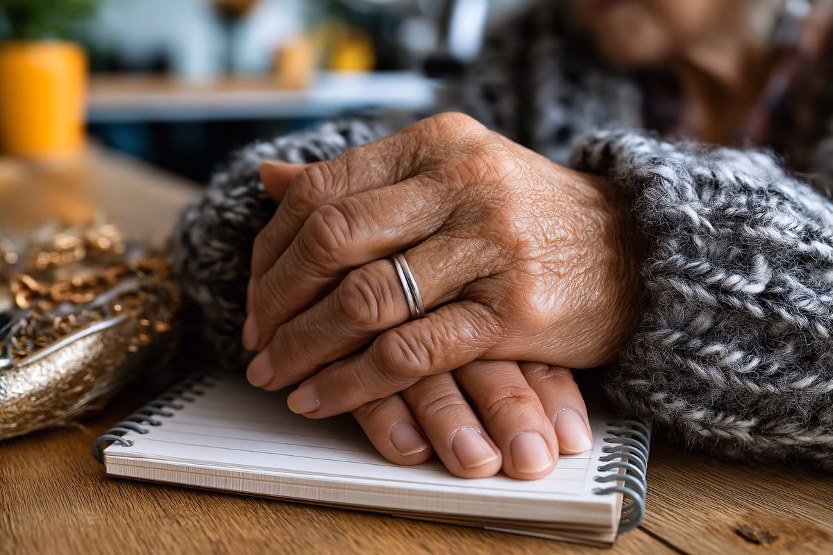 Older hands resting on a household budget notebook and a small purse on a kitchen table.