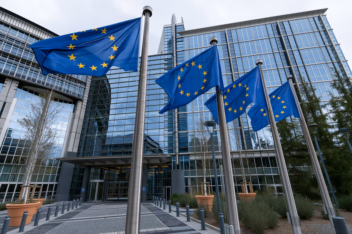 European Union flags on flagpoles in front of a modern glass building.