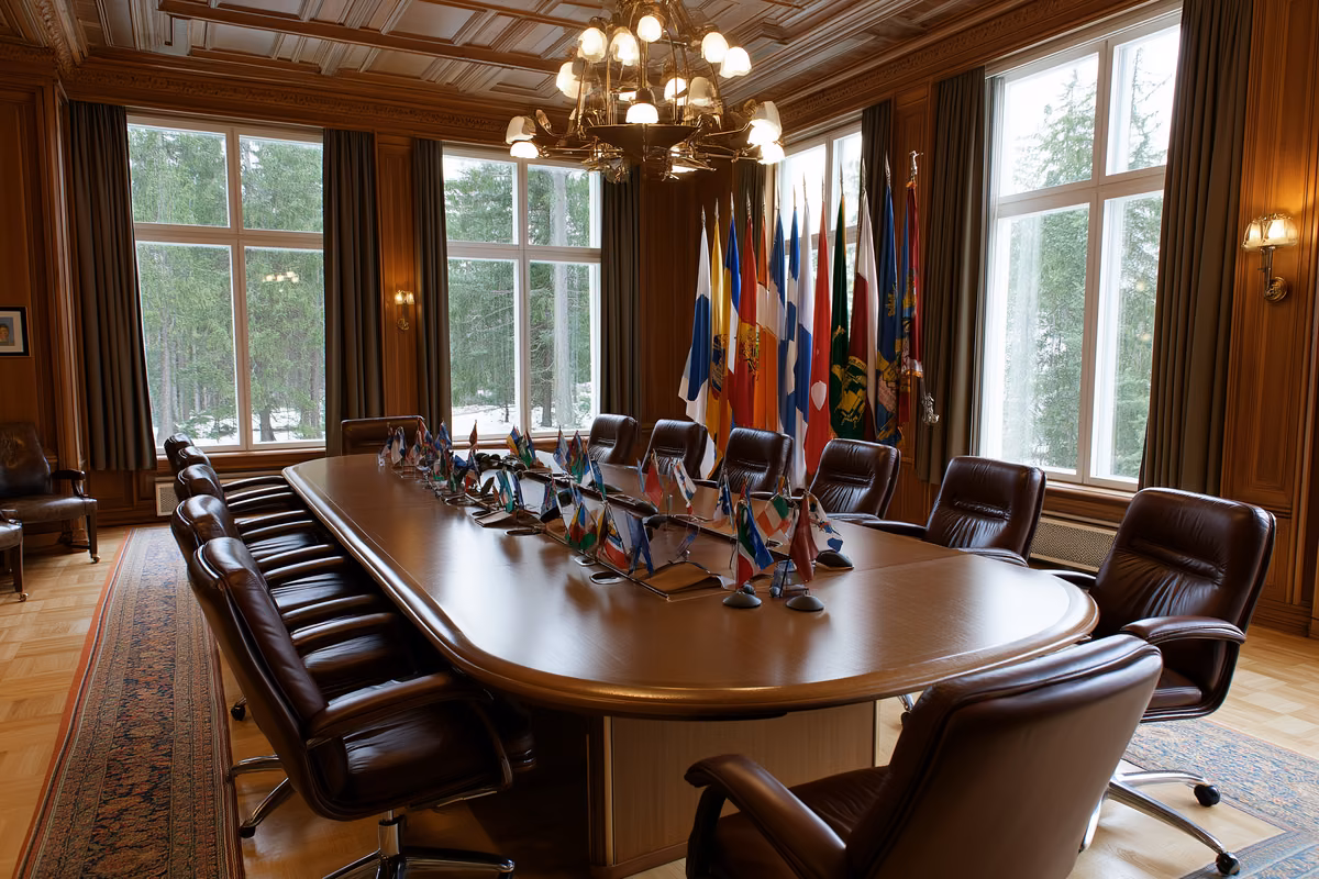 An empty cabinet meeting room with a long oval table, leather chairs and small national flags in morning light